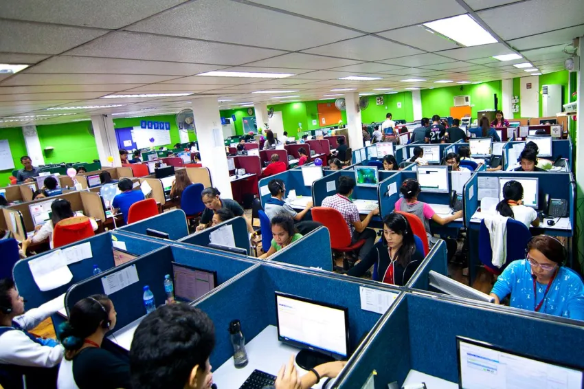 Wide-angle view of busy Philippine call center office with multiple employees working at computer workstations in colorful cubicle environment.