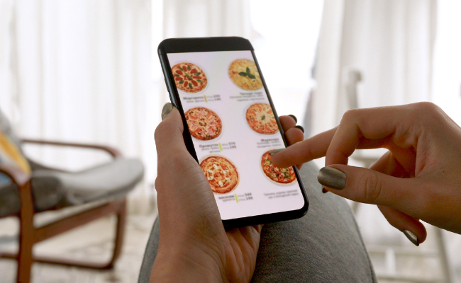 A person holding a smartphone and browsing a menu of pizzas in an app, illustrating accessibility challenges in UX design when users with disabilities are not considered or accommodated.