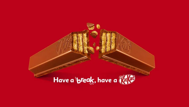 Two Kit Kat chocolate bars breaking apart with crumbs flying on a red background, displaying the famous slogan 'Have a break, have a Kit Kat' in white text.
