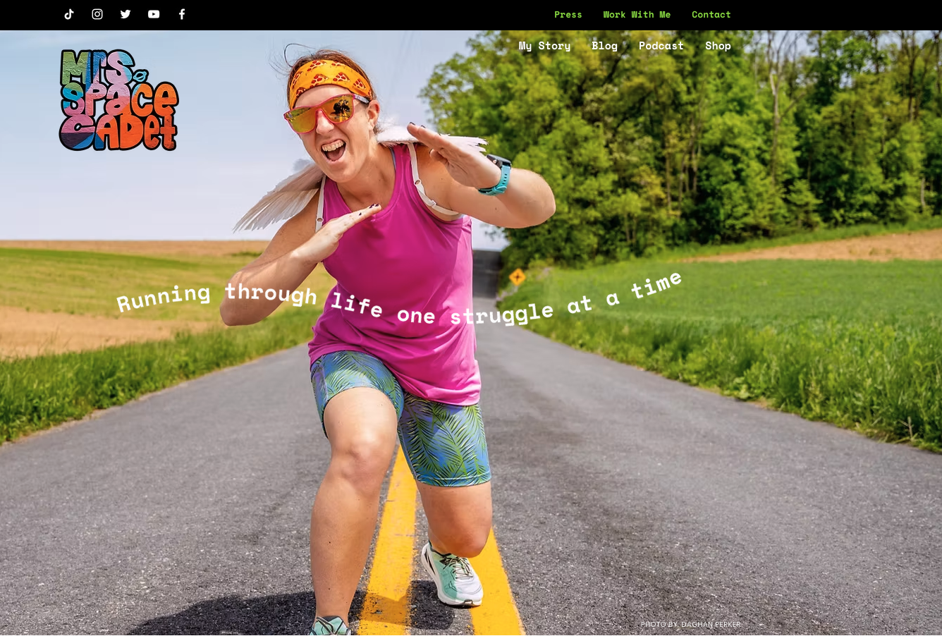 Homepage of Mrs. Space Cadet showing Erin Azar in bright athletic gear posing mid-stride on a road, with the tagline “Running through life one struggle at a time.”