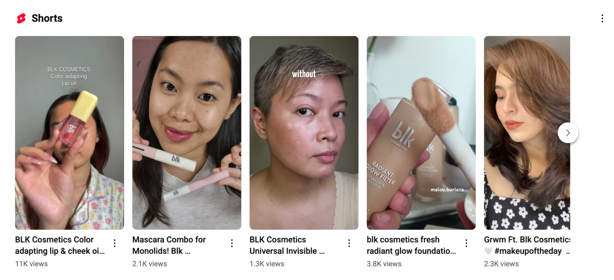 A row of five YouTube Shorts showcases users demonstrating various BLK Cosmetics products such as lip oil, mascara, and radiant glow foundation. Each video includes a thumbnail image of a person applying or holding the product, with views ranging from 1.3K to 11K. The Shorts emphasize product application, texture, and real-life results, engaging viewers through visual tutorials.