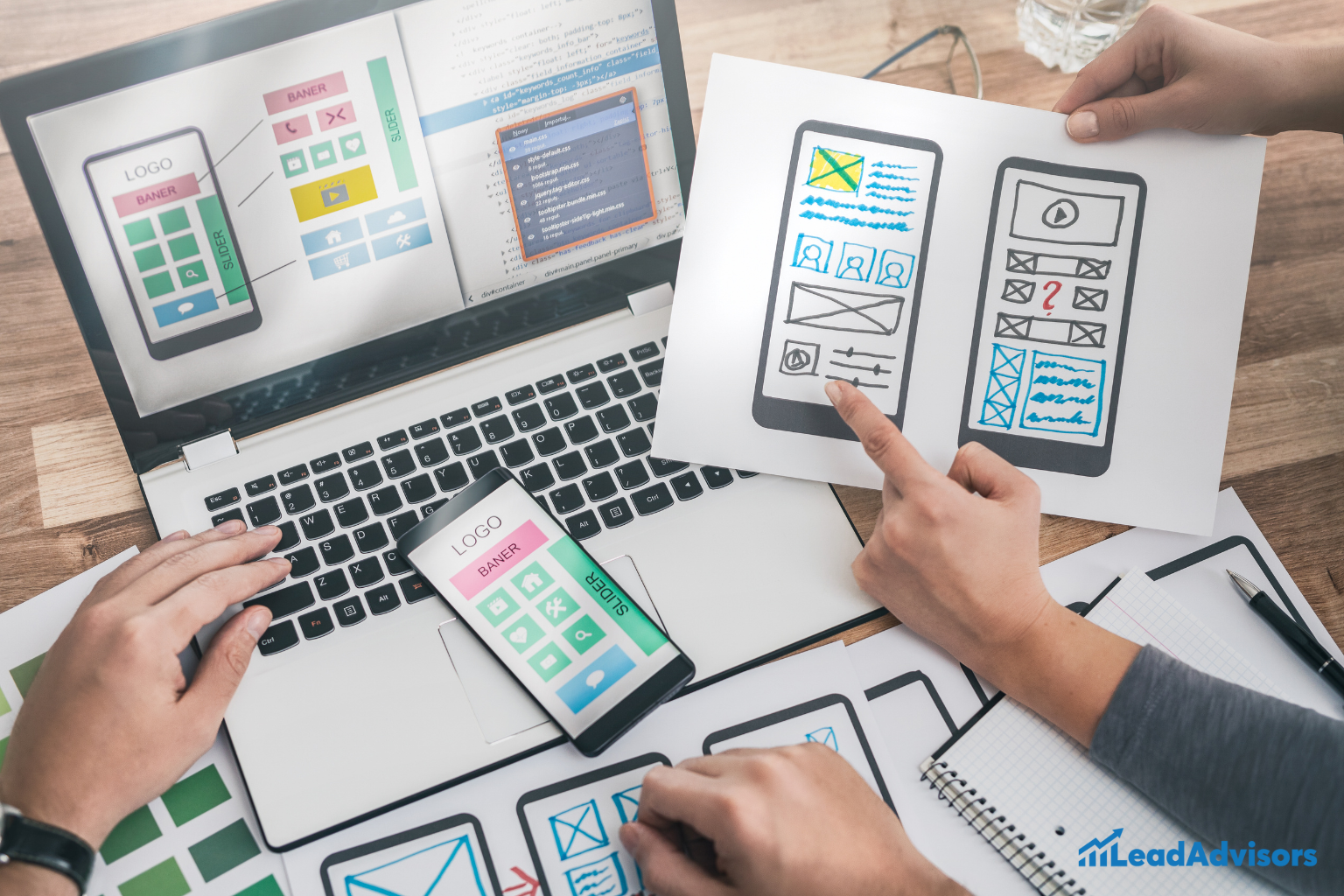 A close-up view of a web design planning session, where team members are reviewing mobile wireframes, design mockups, and layout sketches alongside code displayed on a laptop screen, highlighting the UI/UX development process.