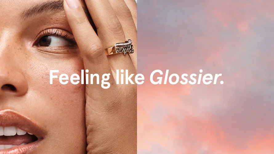 Close-up of a woman’s face next to a soft sky background with the words “Feeling like Glossier” in a minimalist ad.