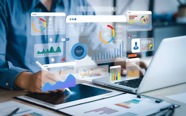Person working on a tablet and laptop surrounded by floating digital dashboards showing graphs, charts, and analytics representing AI-driven marketing tools.
