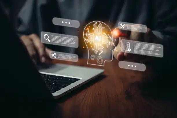 Person using a laptop with a glowing AI head icon and floating digital interface elements representing data and technology concepts.