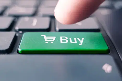 Finger about to press a green keyboard key labeled "Buy" with a shopping cart icon, symbolizing online purchasing.