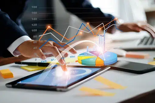 Businessperson using a tablet with overlaid digital charts and graphs representing data analytics and financial performance.