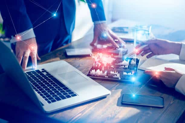 Business professionals discussing data on a tablet and laptop with digital graphics representing AI and data analytics overlaying the scene.