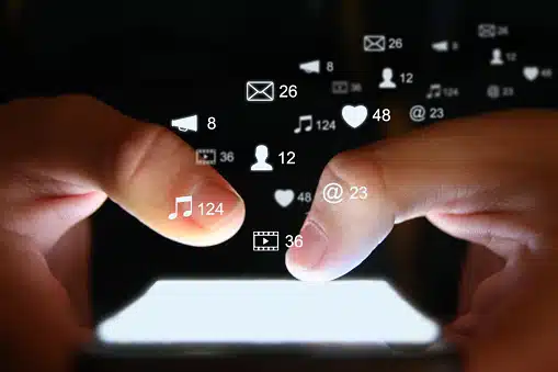 Close-up of hands using a smartphone with floating social media and communication icons, representing digital engagement and local SEO.