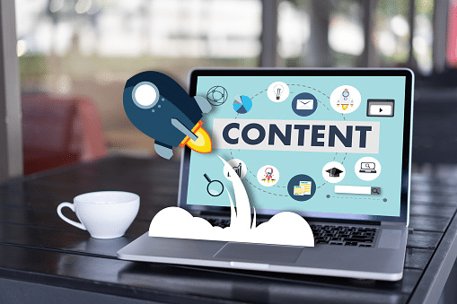Laptop displaying the word "CONTENT" with various digital marketing icons and a rocket graphic launching from the keyboard, symbolizing content growth and promotion.