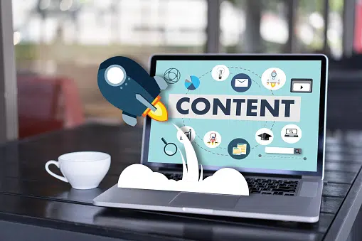 Laptop displaying the word "CONTENT" with various digital marketing icons and a rocket graphic launching from the keyboard, symbolizing content growth and promotion.