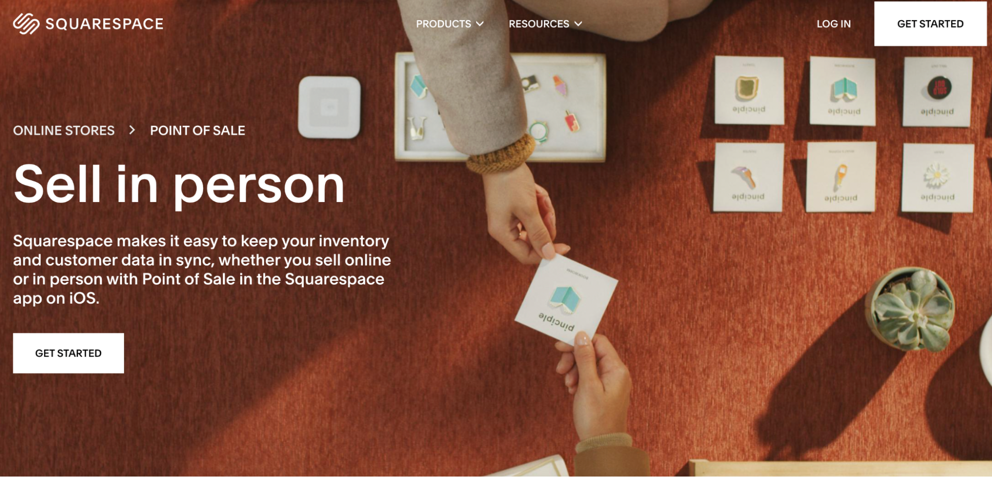 Two people arrange product cards and a card reader on a rust-colored table. The text highlights Squarespace’s in-person point of sale feature, ideal for selling products and syncing inventory—perfect for those considering Shopify vs Squarespace.