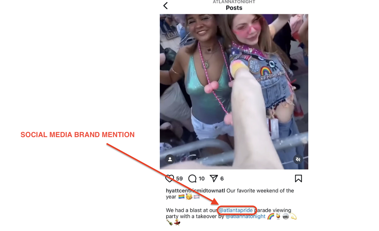 Two women smiling and posing at a crowded outdoor event in casual festival outfits with beads. A hand points toward them. Text on image displays @atlantapride as a Brand Mention in the caption, celebrating community and visibility.