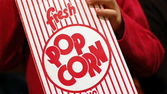 A person holds a red-and-white striped popcorn box labeled “fresh popcorn.