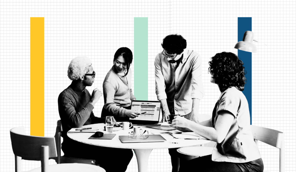 Four professionals gathered around a table reviewing data on a laptop, representing a cross-functional enterprise SEO team working on technical and content strategy.