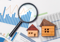 A magnifying glass over graphs and charts with small wooden house models, representing real estate SEO and improved search rankings