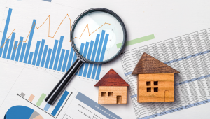 A magnifying glass over graphs and charts with small wooden house models, representing real estate SEO and improved search rankings